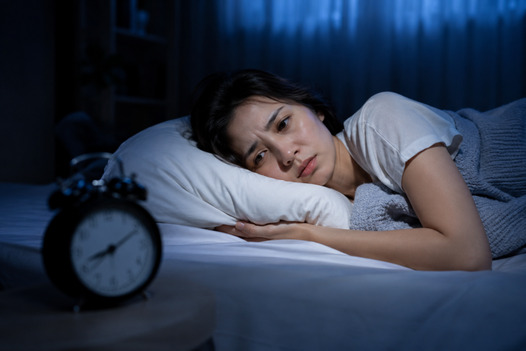 A woman struggling with insomnia looking at an alarm clock in a dark bedroom.